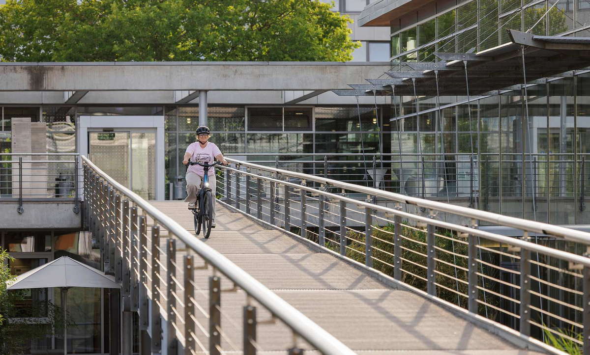 CUBE Supreme Hybrid 2027: Fahrt über einen Steg zwischen Glasgebäuden