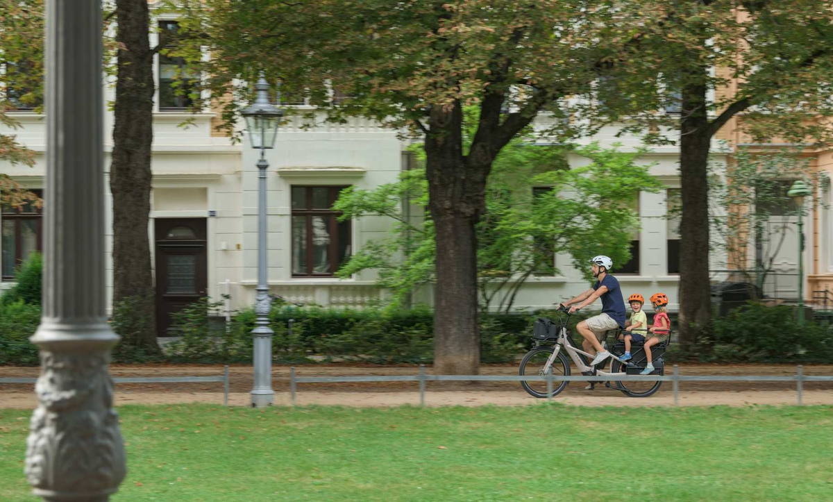 CUBE Transport E-Bikes 2027: Fahrt durch einen Park mit zwei Kindern auf dem Heckträger