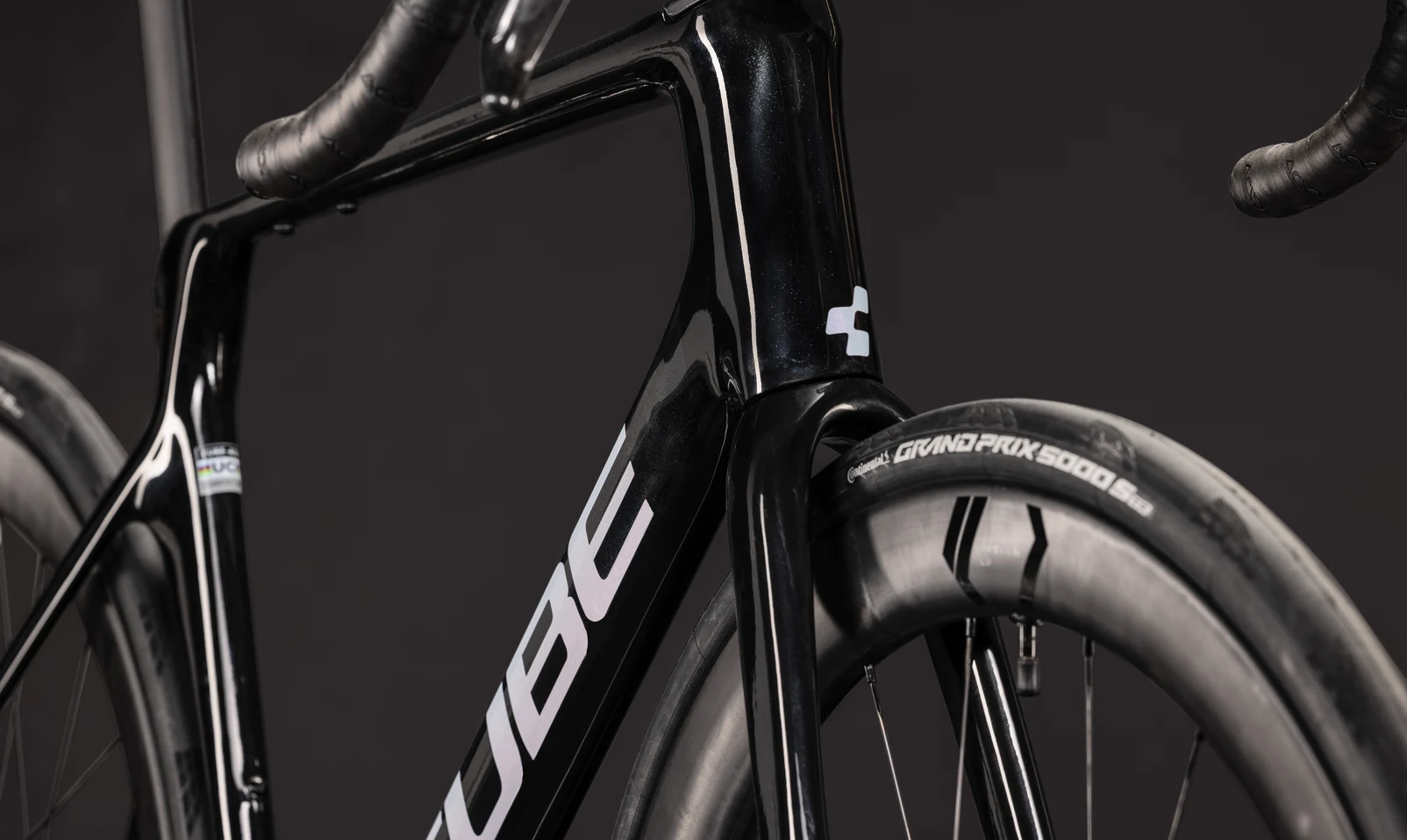 Steuerrohr und Vorderrad eines CUBE Agree C:62 SLT AXS 2027 in blackpearl´n´switchwhite, das CUBE-Logo sitzt am Unterrohr, der Reifen trägt die Aufschrift Grand Prix 5000 S-TR