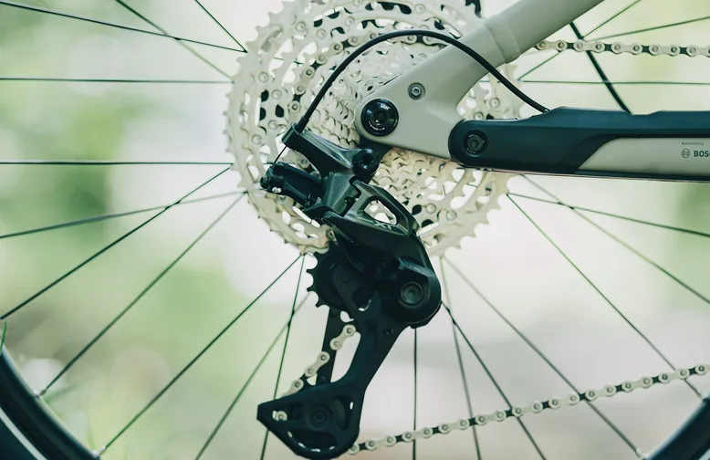 Nahaufnahme von Kassette, Kette und Shimano-Deore-XT-Schaltwerk an einem CUBE Stereo Hybrid ONE44 SLX 800, davor die Speichen des Hinterrads, dahinter grüner unscharfer Hintergrund