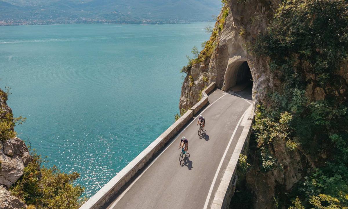 CUBE Fahrräder 2027: zwei Rennradfahrer auf einer Uferstraße hoch über einem türkisen See