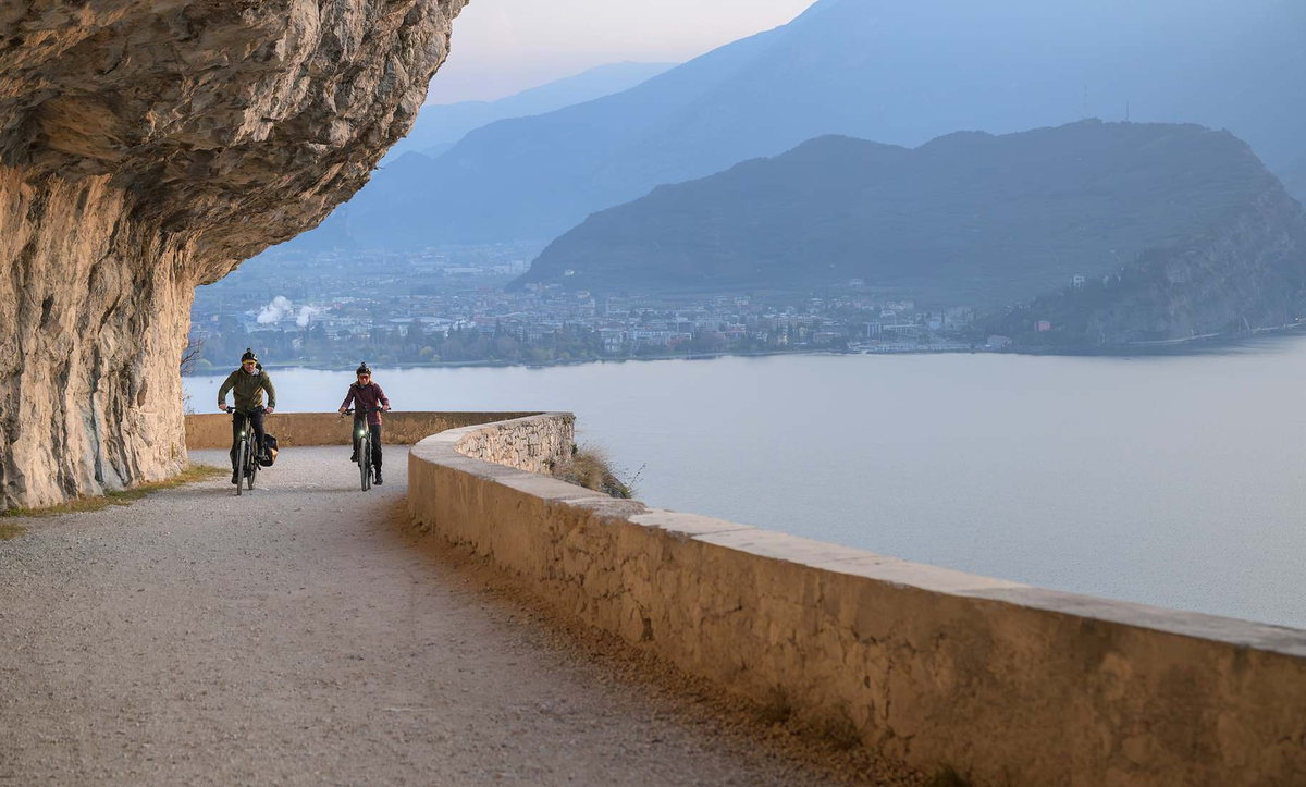 CUBE Kathmandu Hybrid ONE11 2027: zwei Fahrer mit Gepäck auf einem Felsweg über einem Bergsee