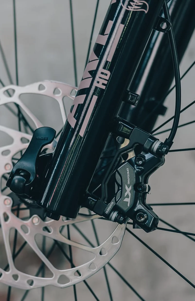 Vorderrad des CUBE Stereo Hybrid ONE22 SLX 800 2027, schwarze Federgabel mit Bremsscheibe und Bremssattel Shimano Deore XT, dahinter eine helle Mauer