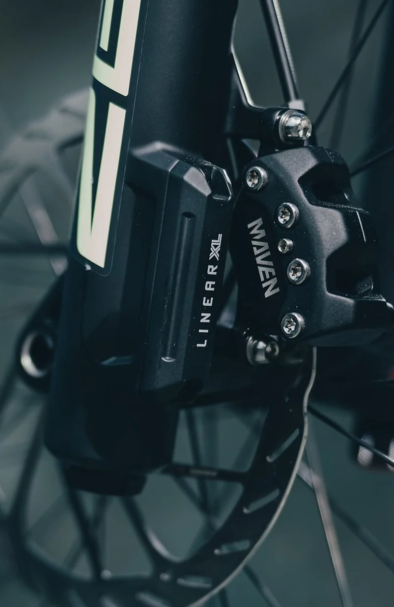 Bremssattel einer Sram Maven am CUBE Stereo Hybrid ONE77 TM 2027, schwarzer Sattel mit dem Schriftzug MAVEN, verschraubt am schwarzen Gabelholm, dahinter die Bremsscheibe und die Speichen des Vorderrads