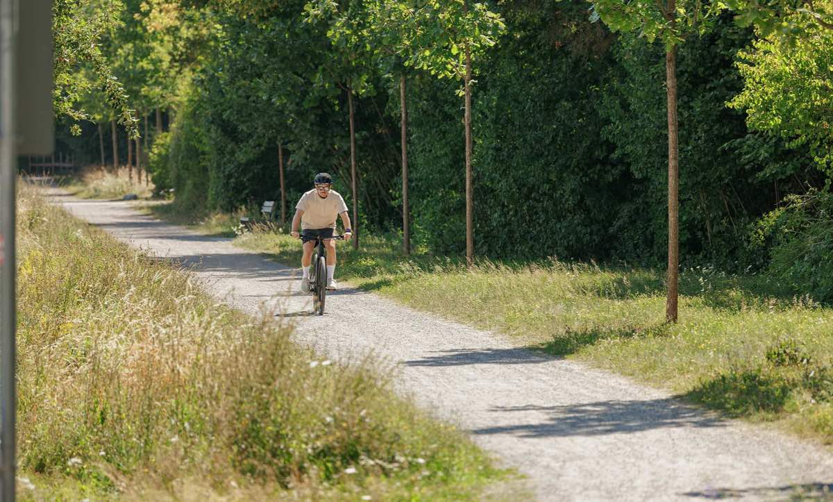 CUBE Nulane 2027: Fahrt auf einem sonnigen Schotterweg zwischen Wiese und Hecke